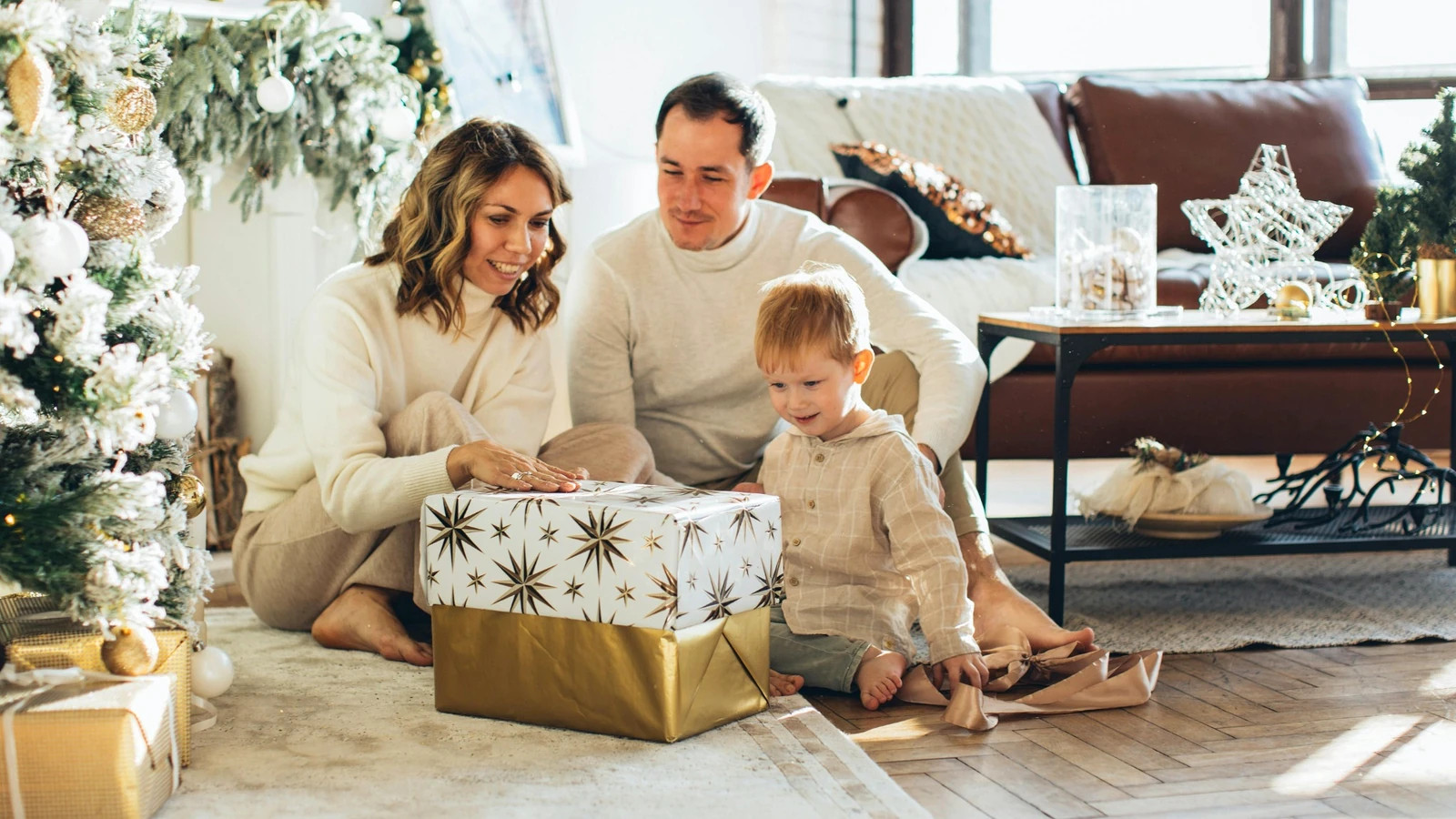 Rodina s malým dítětem rozbaluje vánoční dárek v obýváku