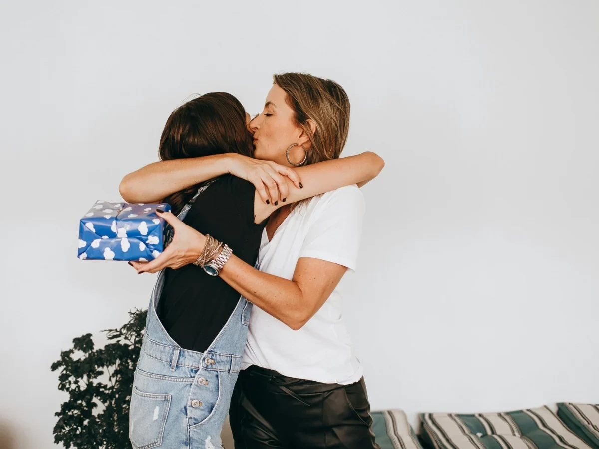 Maminka objímá dceru a drží modře zabalený dárek